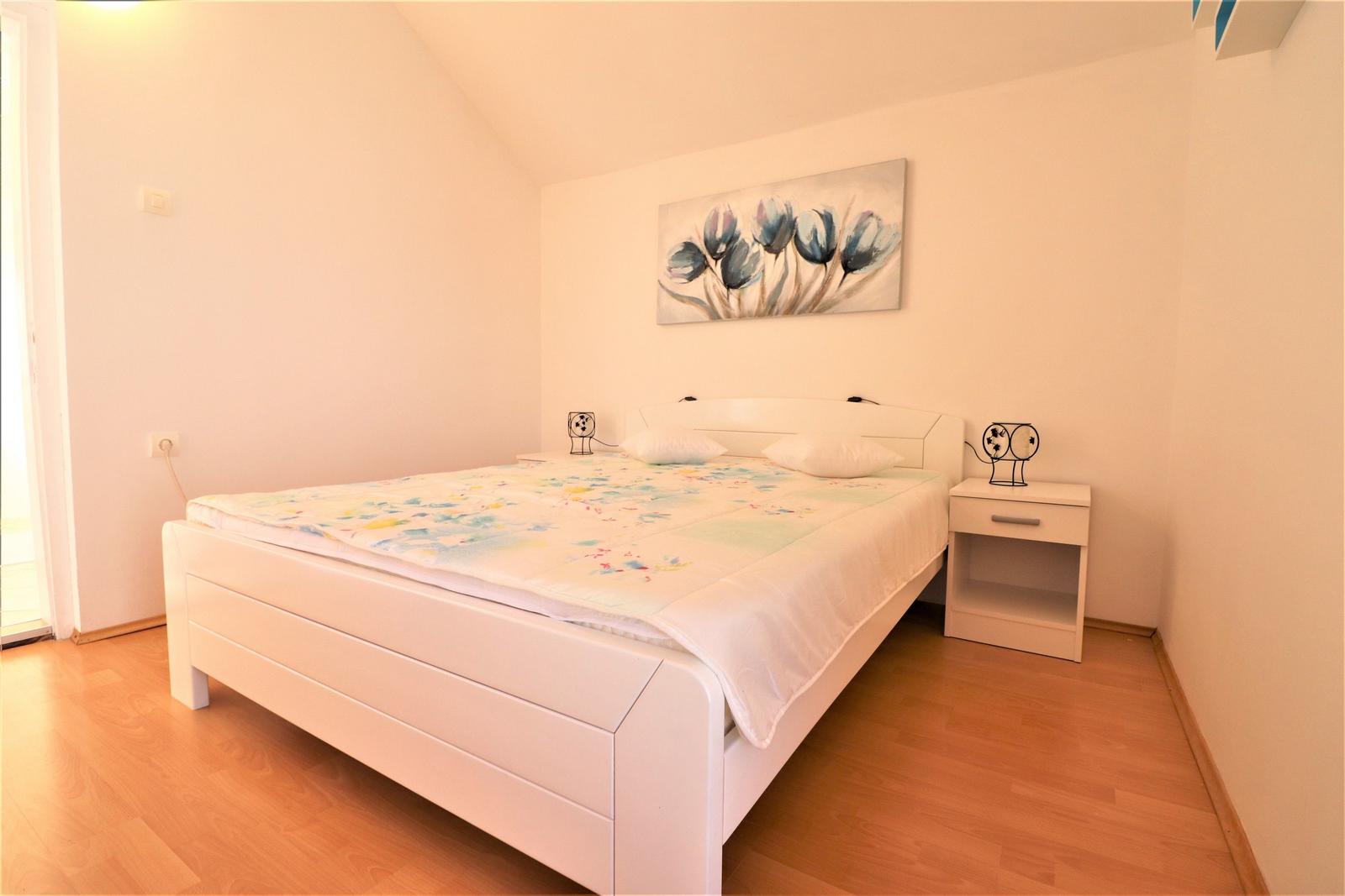 Schlafzimmer mit weißem Bett, Nachttisch und Wandbild mit Tulpenmotiv.