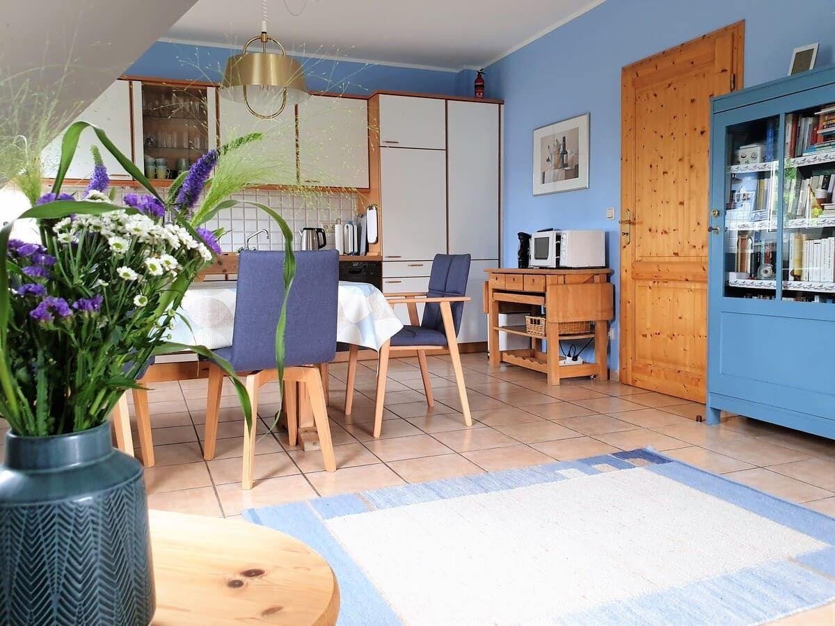 Essbereich mit Tisch, Stühlen und Küchenzeile. Blaue Wände, Holzmöbel und Blumen.