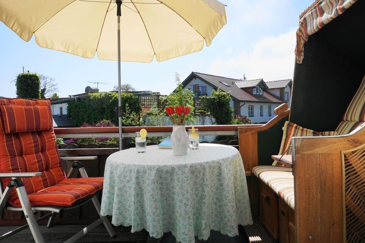 Terrasse mit Tisch, Stühlen und Sonnenschirm. Blick auf Wohnhäuser und Grünflächen.