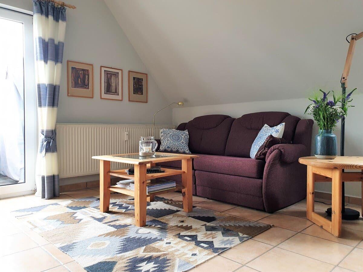 Wohnzimmer mit Sofa, Holztisch und Teppich. Fenster mit Vorhängen und Bilder an der Wand.