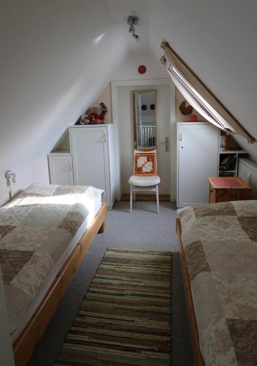 Zwei Betten, Schrank, Stuhl und Fenster in einem Dachzimmer.
