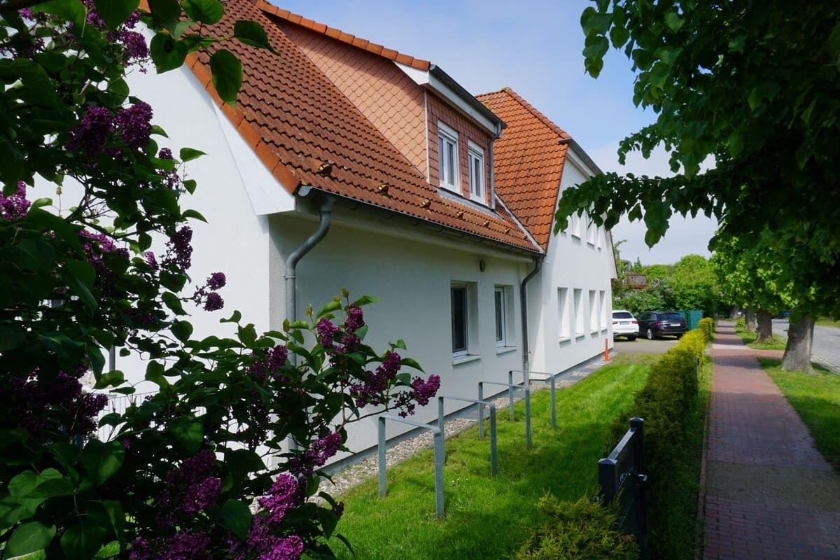 Weiße Villa mit rotem Dach, umgeben von grüner Wiese und blühenden Lilien.