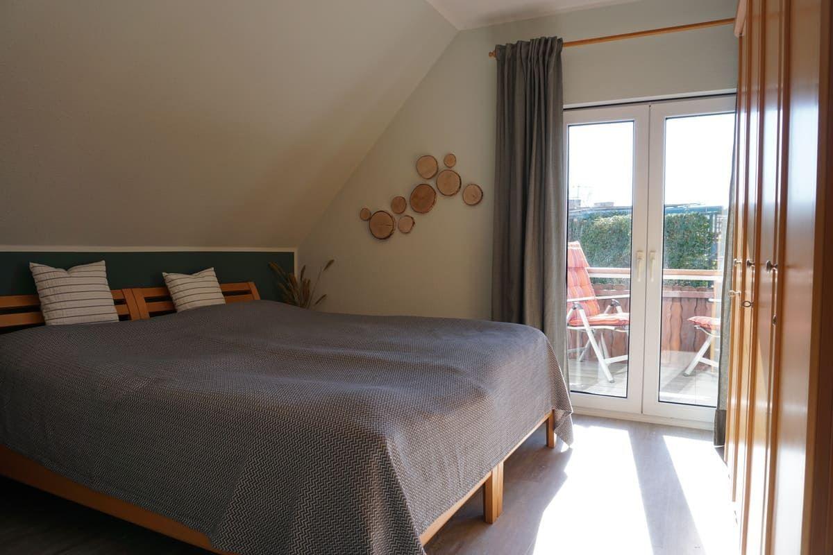 Schlafzimmer mit Dachschräge, Bett, Balkonzugang und Holzregal.