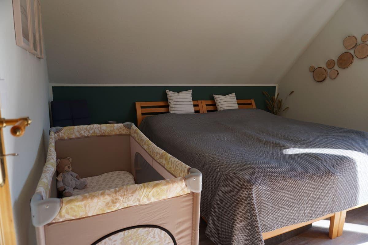 Schlafzimmer mit Doppelbett und Babybett. Wand mit Holzscheiben. Dachneigung sichtbar.