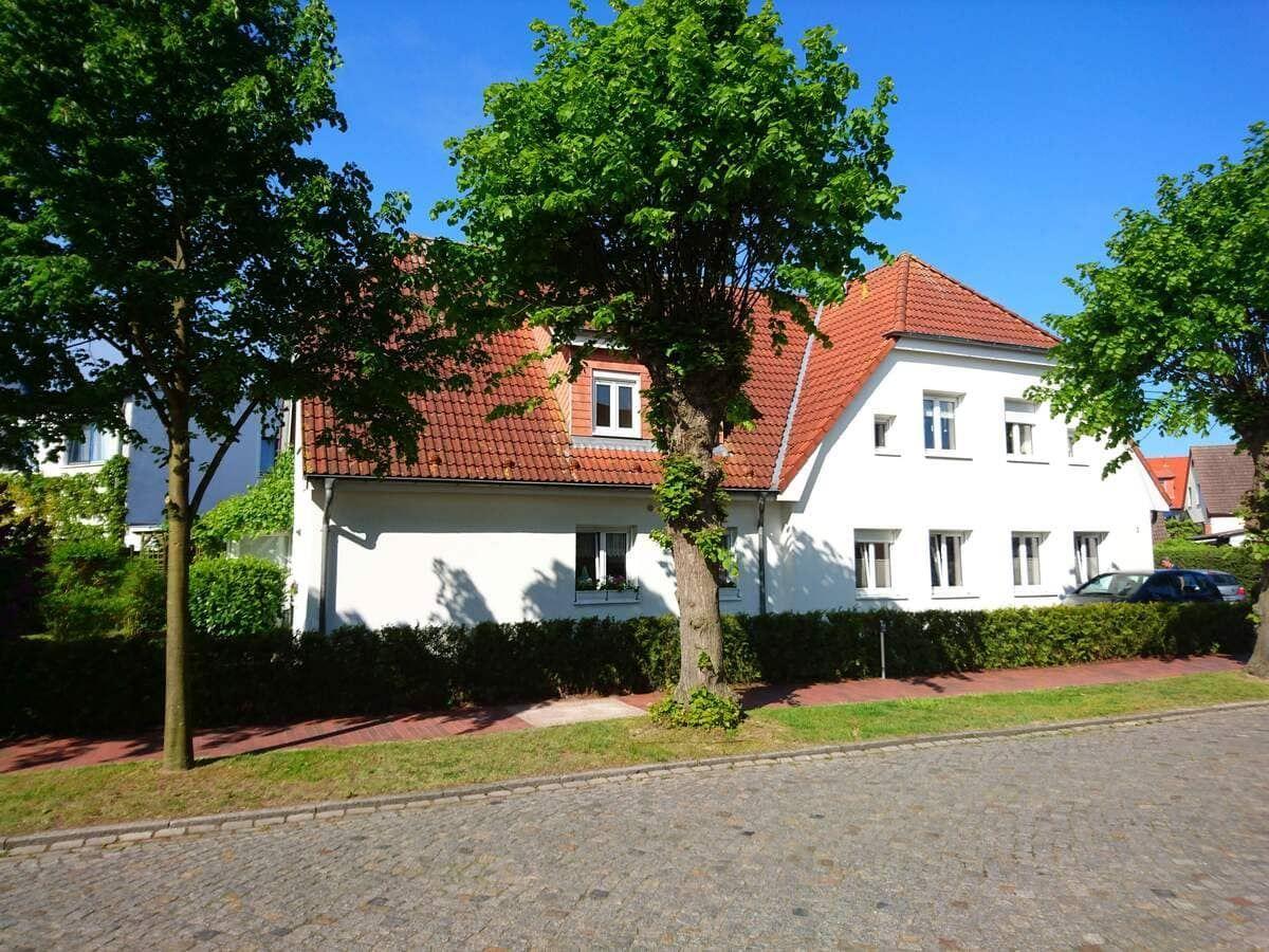 Weiße Villa mit rotem Dach und Bäumen im Vorgarten.