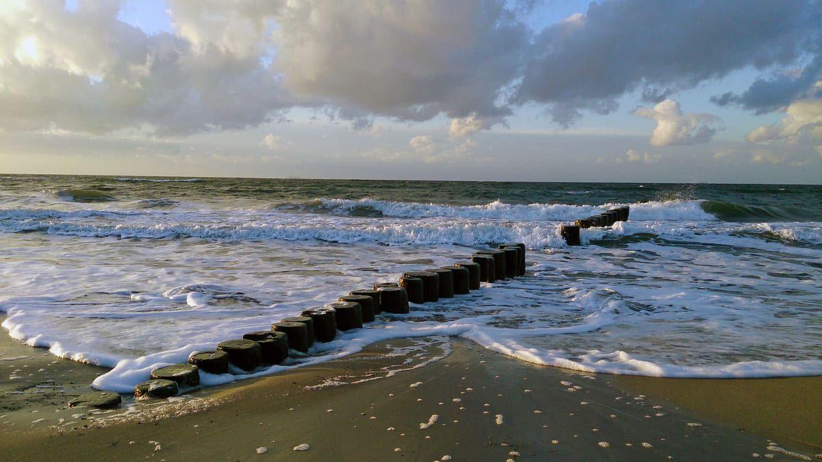 Strand mit Wellen und Holzpfosten entlang des Wassers.