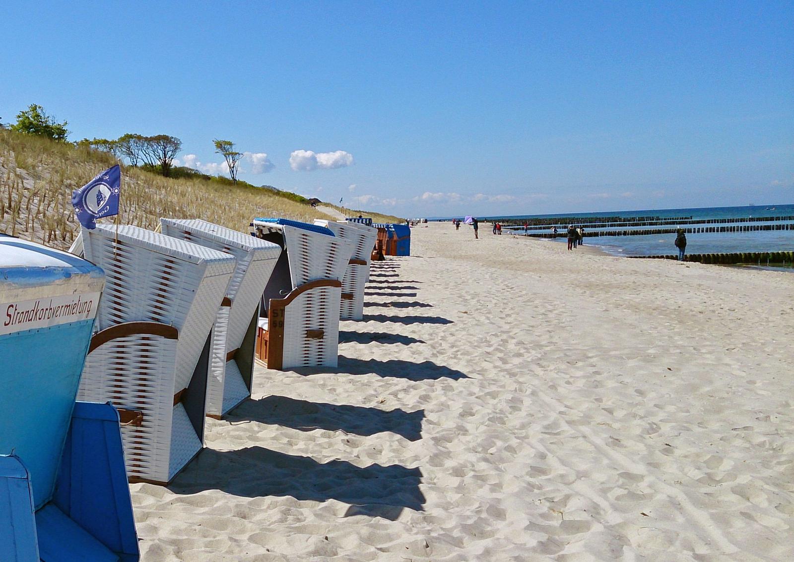 Strandkörbe stehen am Strand, im Hintergrund das Meer und Dünen.