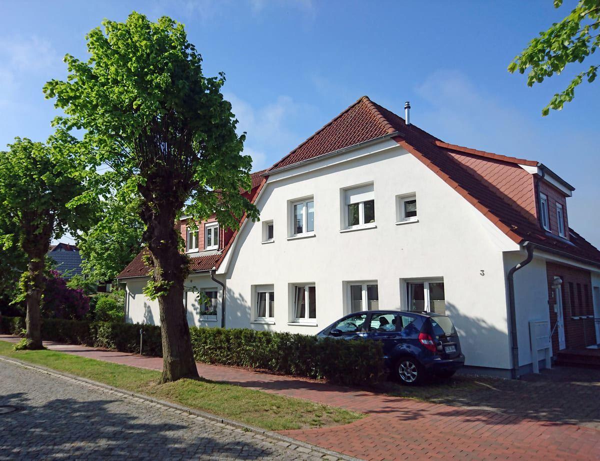 Weißes Haus mit rotem Dach, umgeben von Bäumen und einem gepflasterten Weg.
