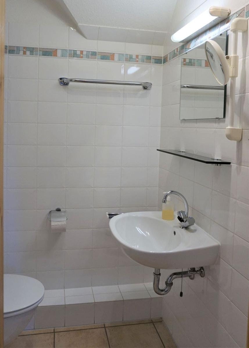 Badezimmer mit Waschbecken, Spiegel, Toilette und Handtuchhalter.