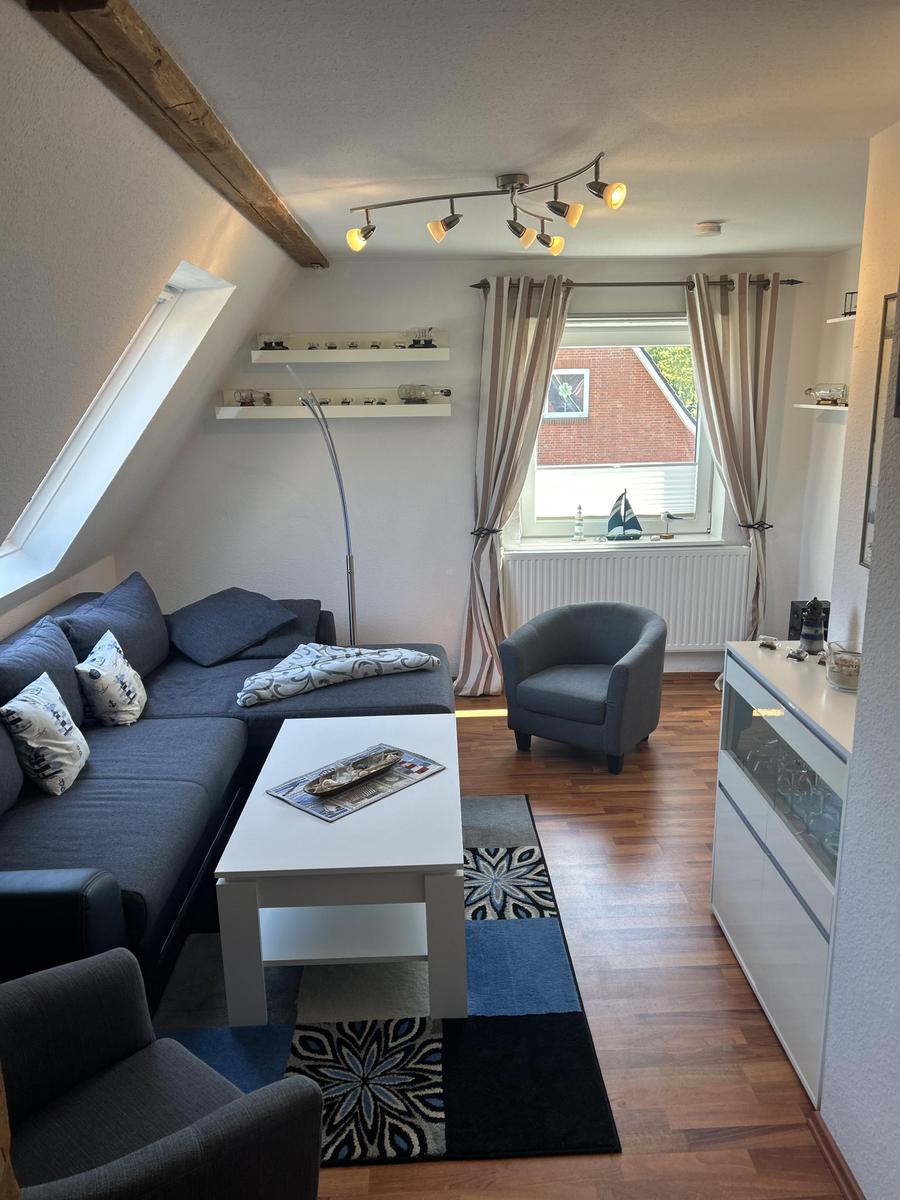 Wohnraum mit Sofa, Sessel und Fenster. Holzdielen und Dachschräge.