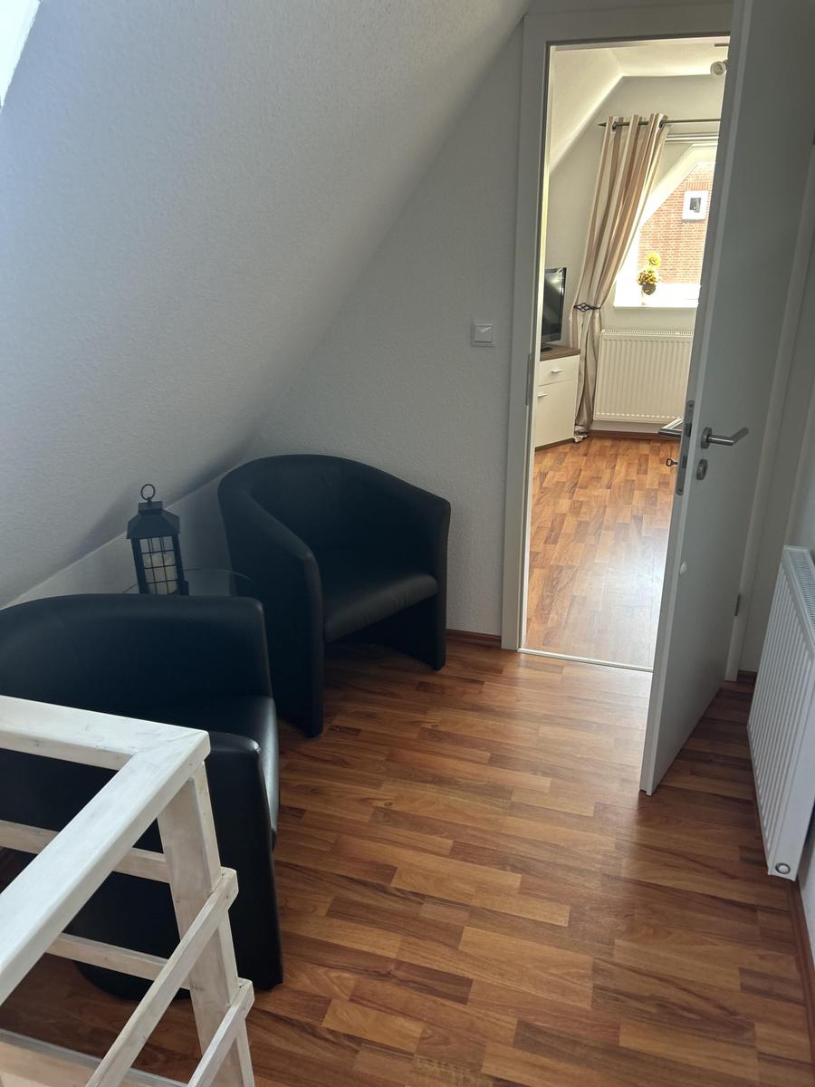 Zimmer mit Holzboden, schwarzen Sesseln und Blick in einen angrenzenden Raum.