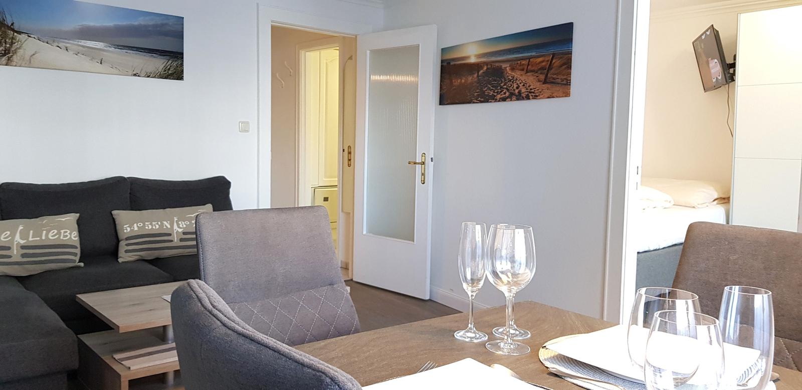 Wohn- und Essbereich mit Sofa, Tisch und Stühlen. Wandbilder zeigen Strandlandschaften.