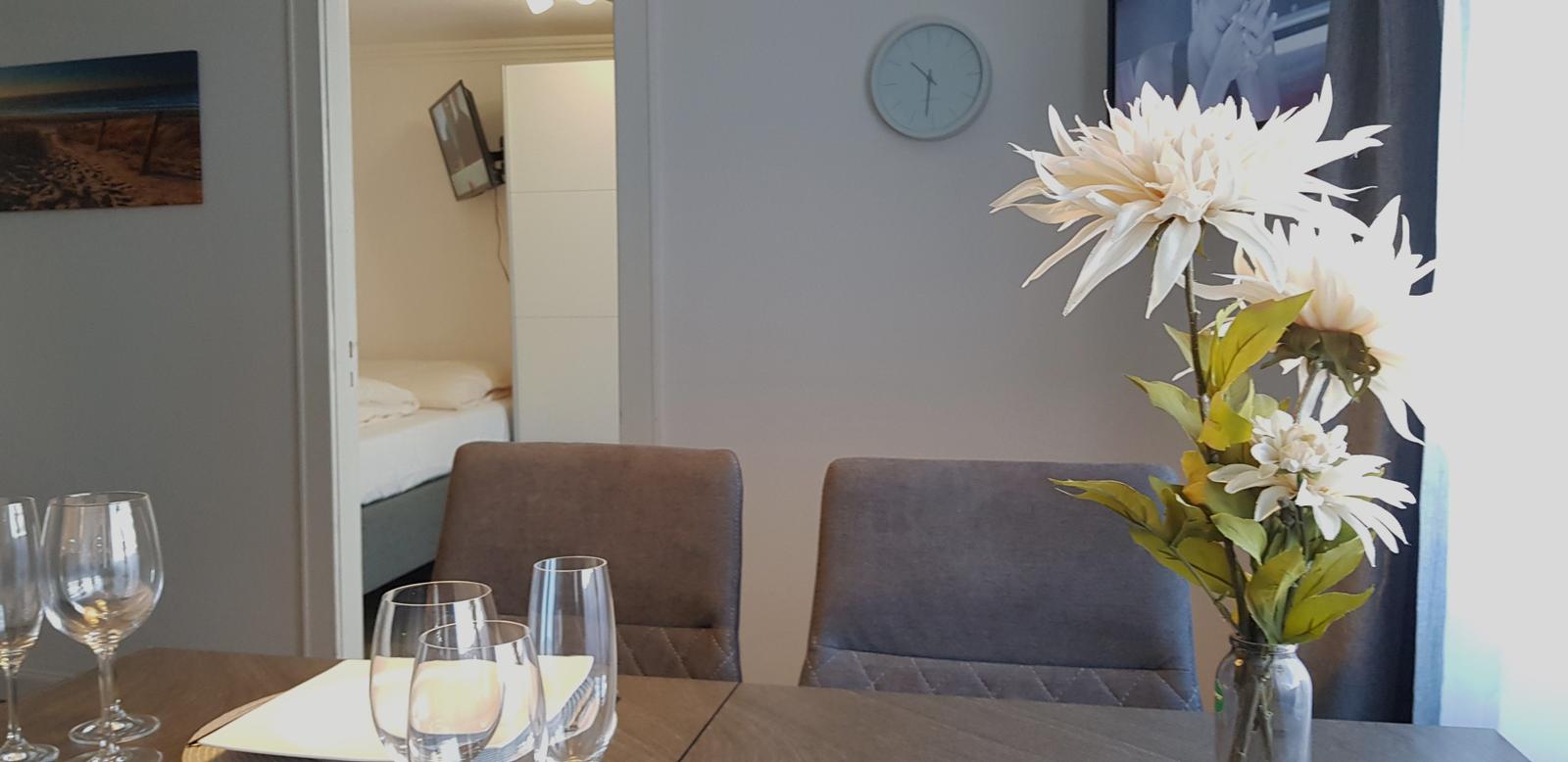 Esstisch mit Gläsern und Blumen, Blick in Schlafzimmer mit Bett und TV.
