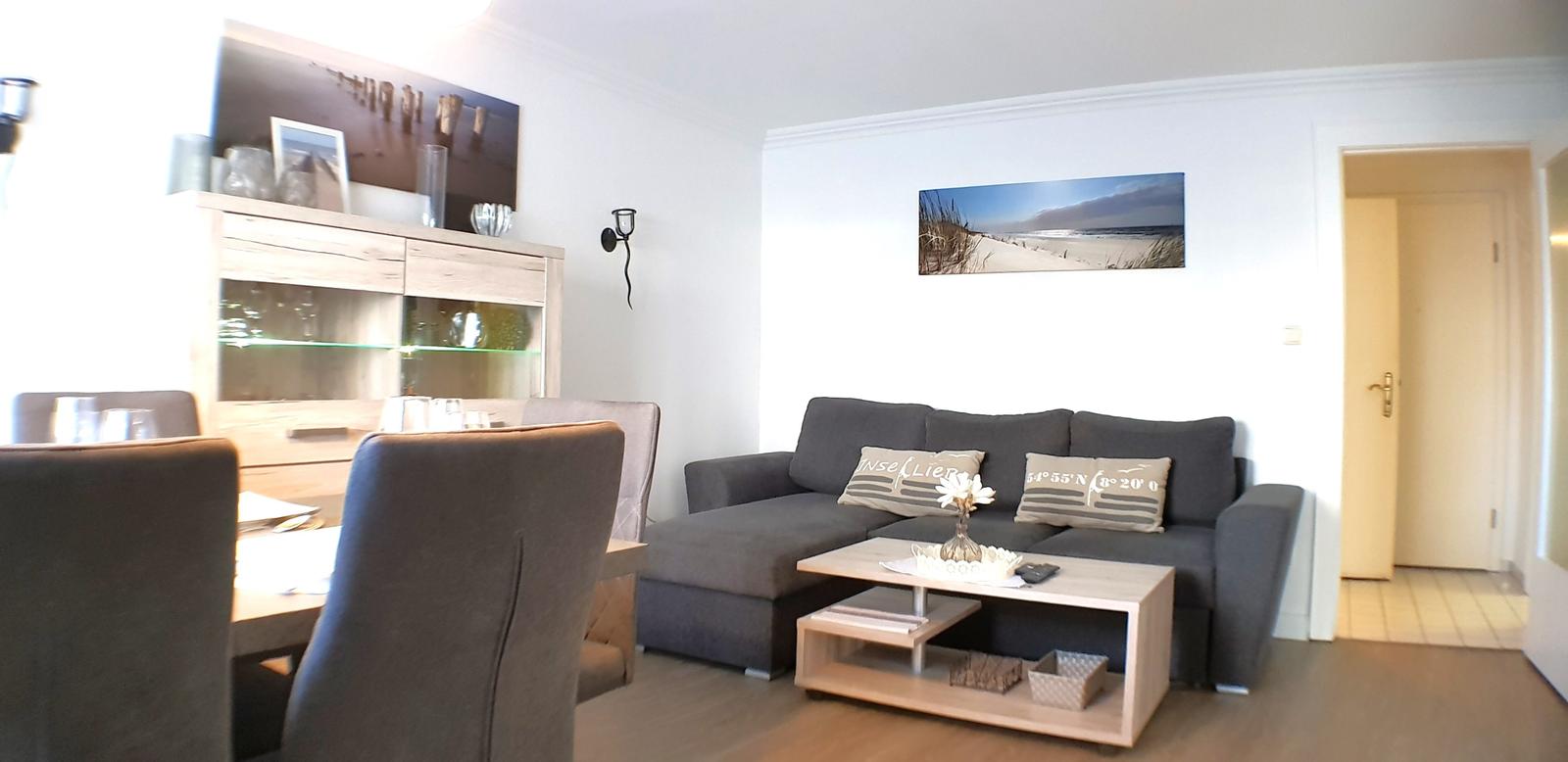 Wohn- und Essbereich mit Sofa, Tisch und Stühlen. Wandbild zeigt Strand.