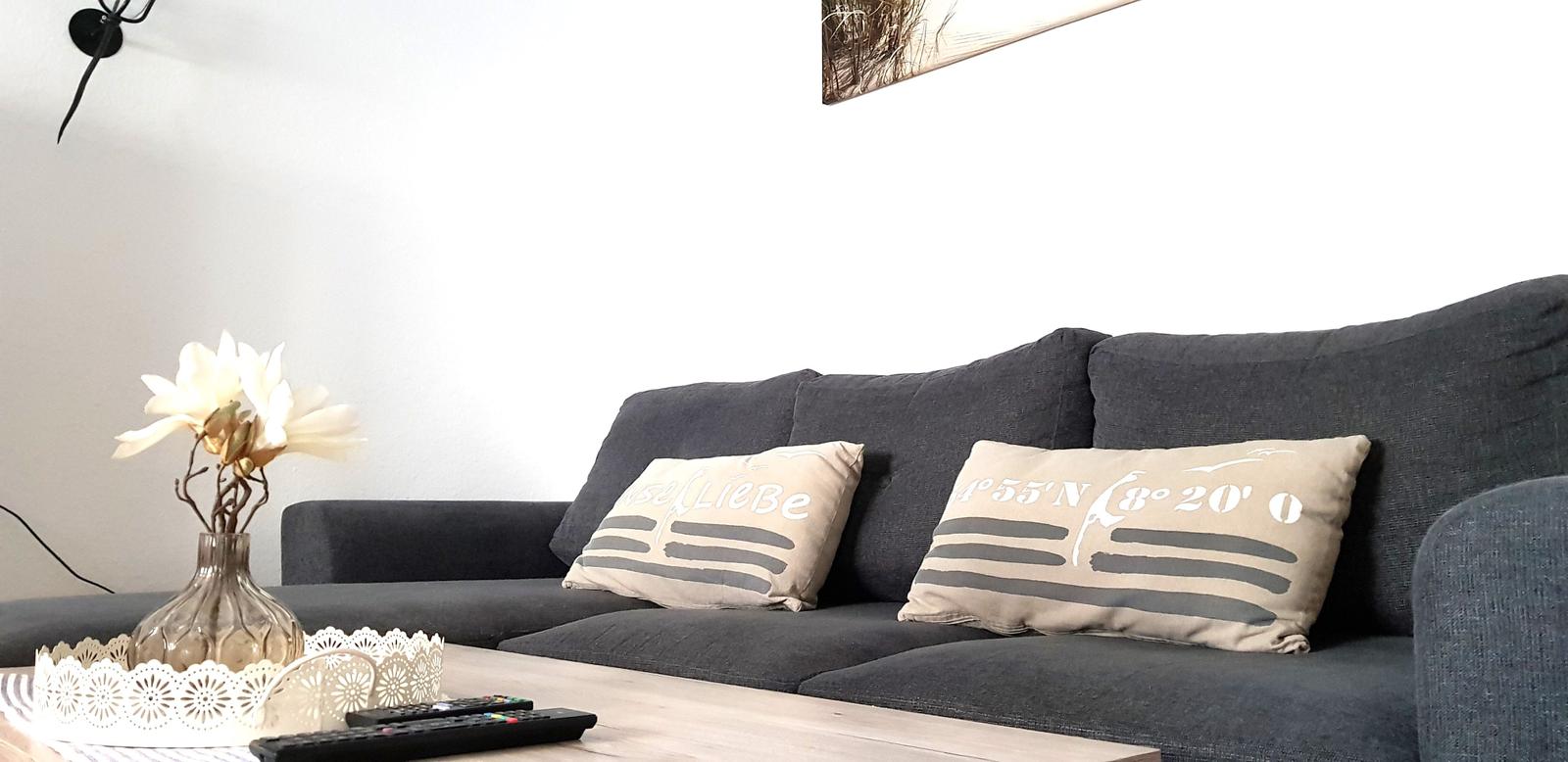 Grauer Sofa mit Kissen und Tisch mit Blumen und Fernbedienung.