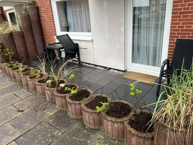 Terrasse mit Sitzgelegenheiten und Pflanzenkübeln entlang der Wand.