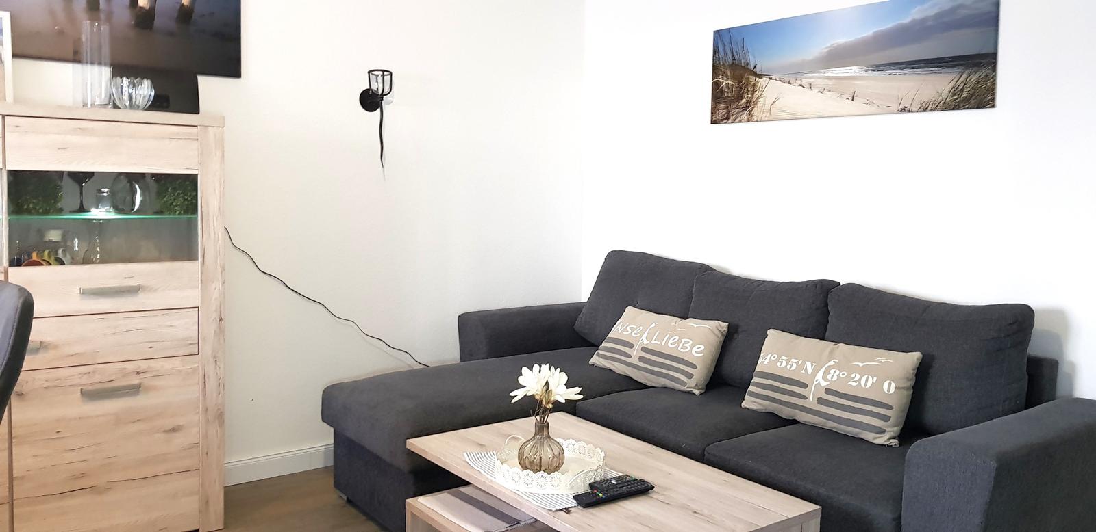 Ein Wohnzimmer mit grauem Sofa, Holztisch und Wandbild