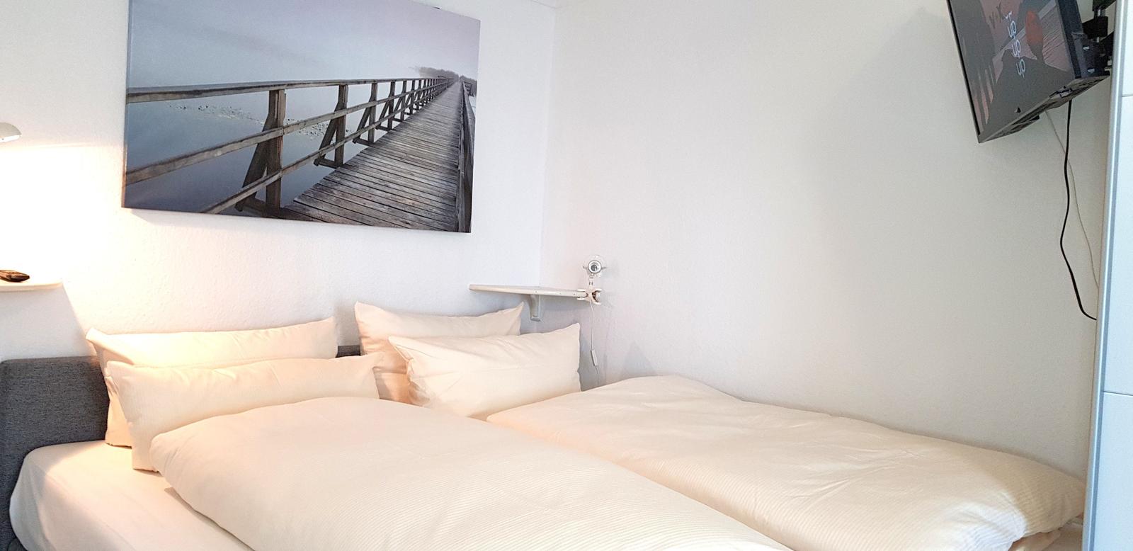 Zwei Betten mit weißen Bettwäsche, Wandbild und TV.