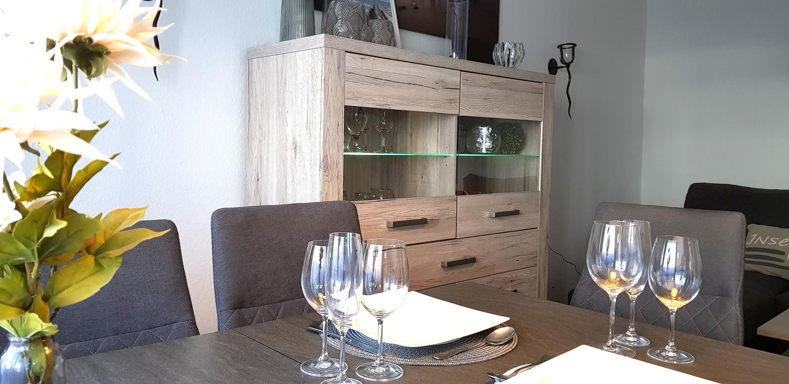 Esstisch mit Gläsern und Blumen vor einem Sideboard.