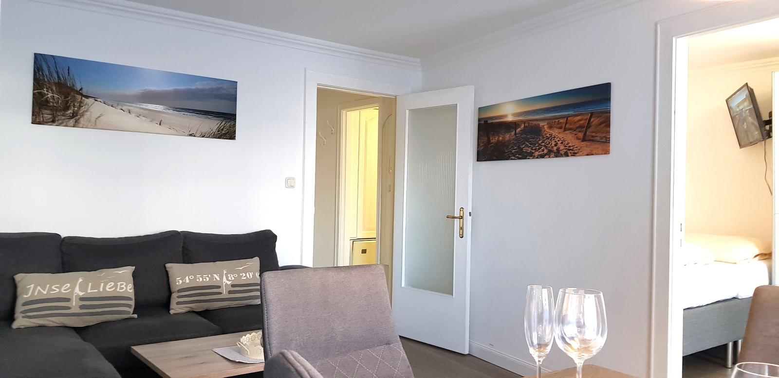Wohnzimmer mit Sofa, Wandbildern und Blick in Schlafzimmer.