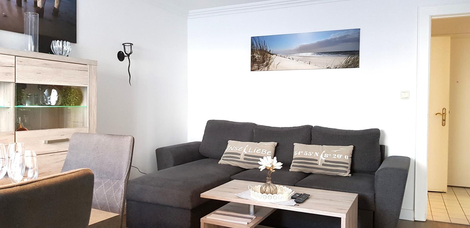 Wohnzimmer mit grauem Sofa, Holztisch und Wandbild von Strand.