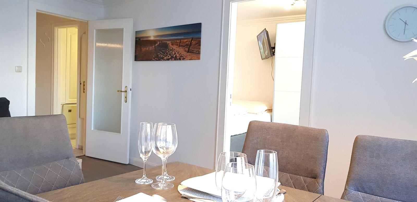 Essbereich mit Tisch, Stühlen und Gläsern. Hintergrund zeigt Schlafzimmer und Flur.
