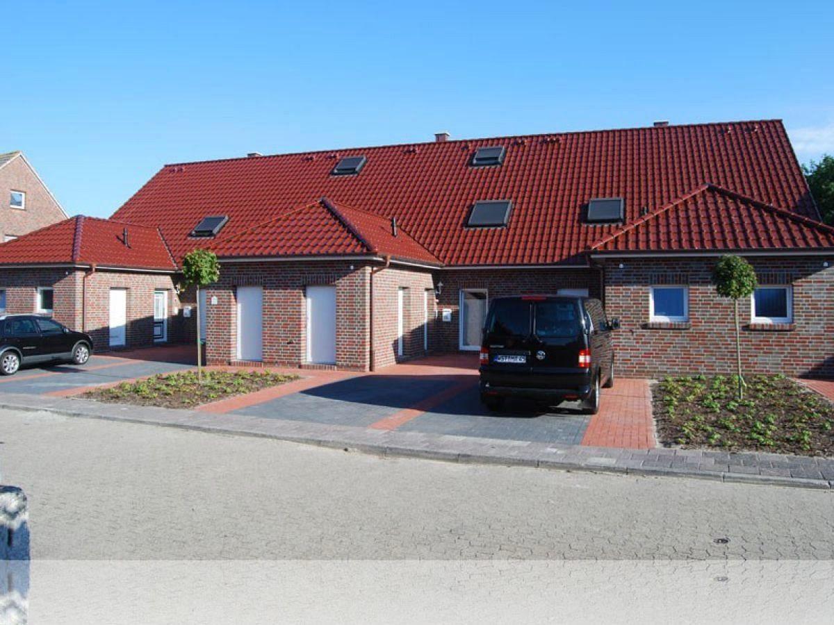Ferienhaus mit rotem Ziegeldach, mehreren Fenstern und Parkplätzen vorne.