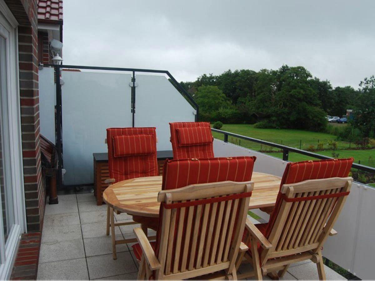 Terrasse mit Holztisch und roten Sitzkissen. Blick auf grünes Gelände.