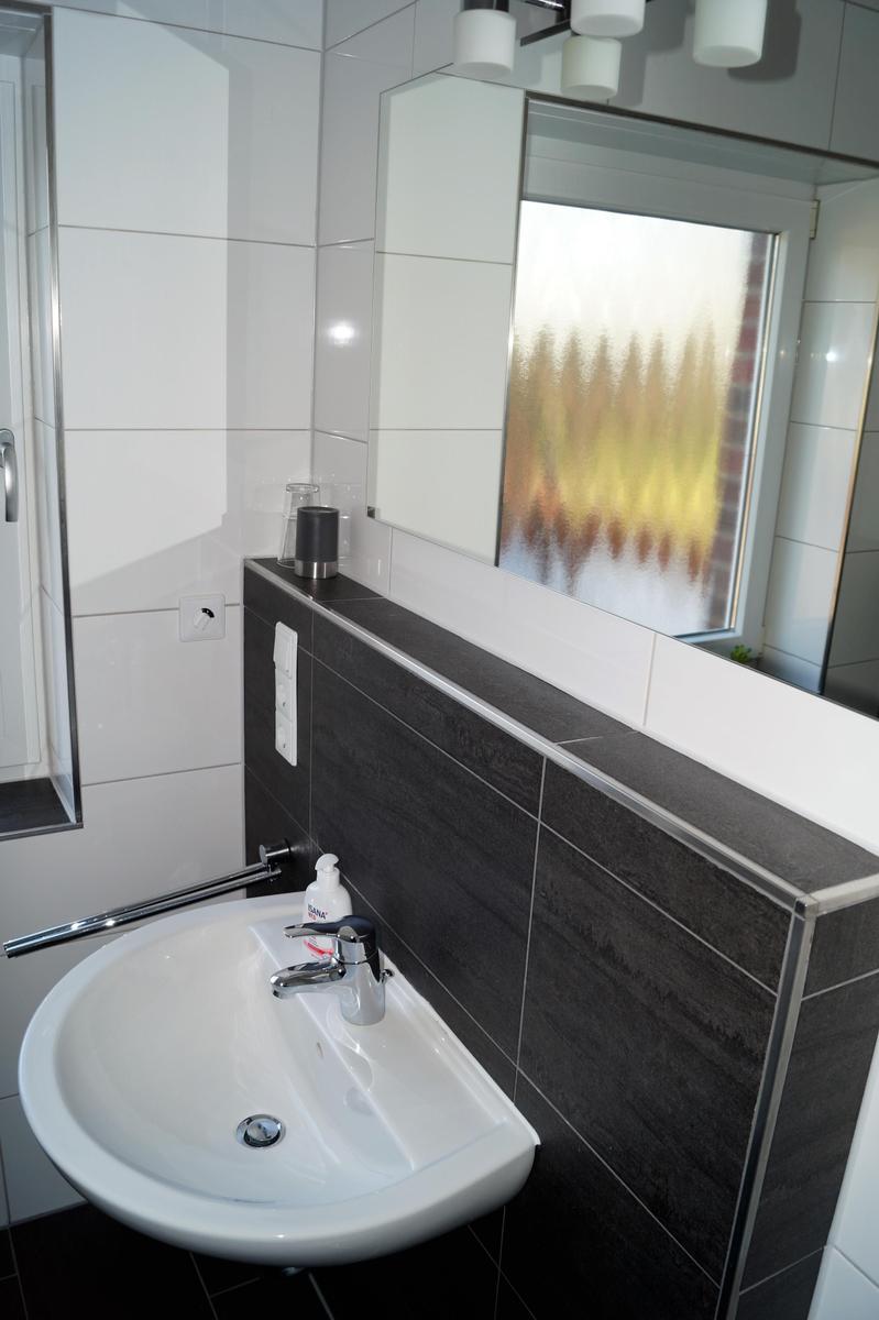 Bad mit Waschbecken, Spiegel und Fenster mit getöntem Glas.