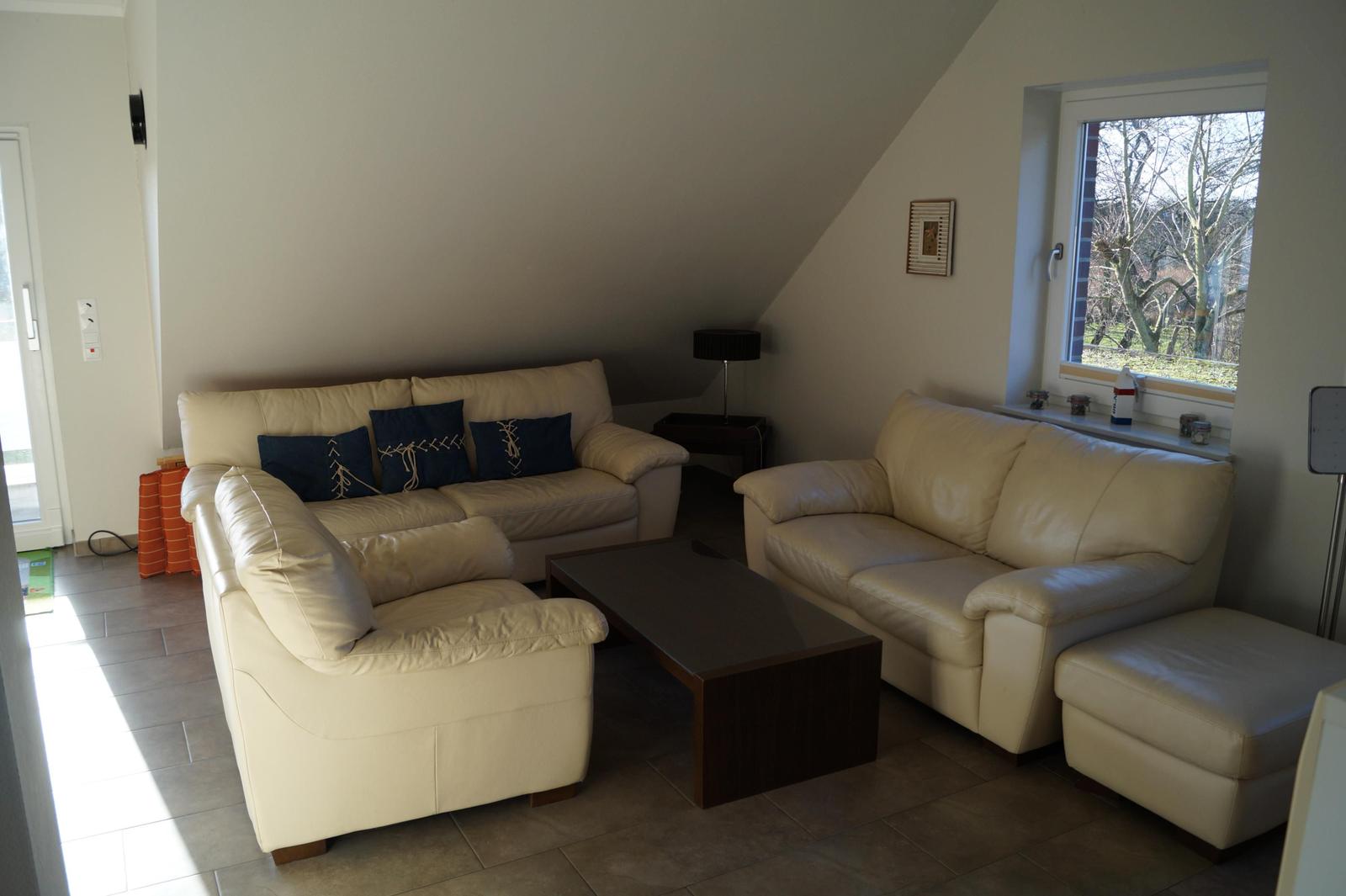 Wohnzimmer mit cremefarbenen Ledersofas, Holztisch und Fenster mit Blick auf Bäume.