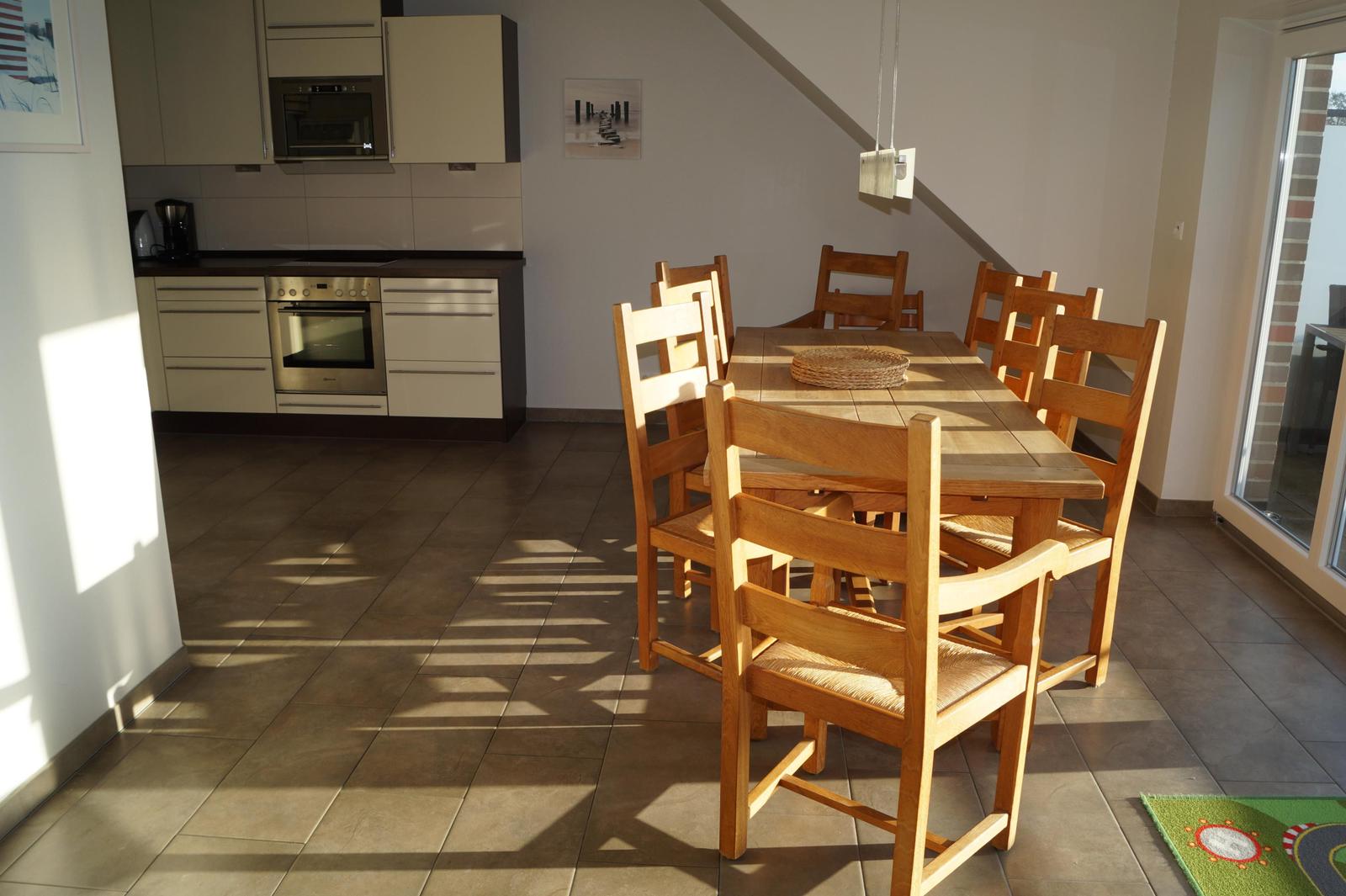 Essbereich mit Holztisch und Stühlen, Küche mit Edelstahlgeräten und Fliesenboden.