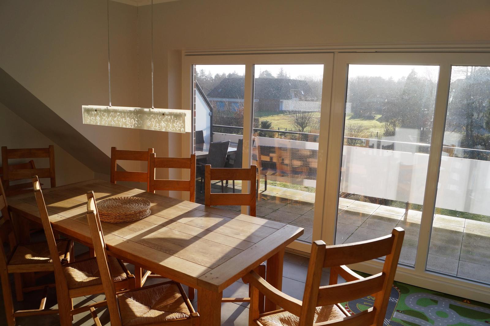 Esszimmer mit Holztisch, Stühlen und Blick auf Balkon.