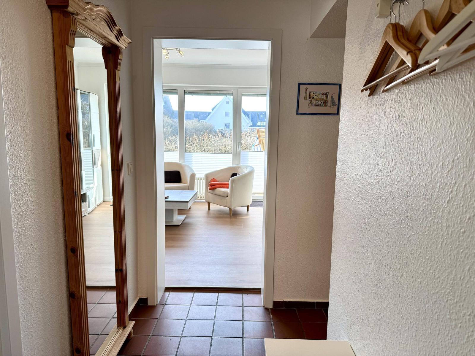 Eingangsbereich mit Spiegel und Blick in Wohnzimmer mit Sitzgelegenheiten.