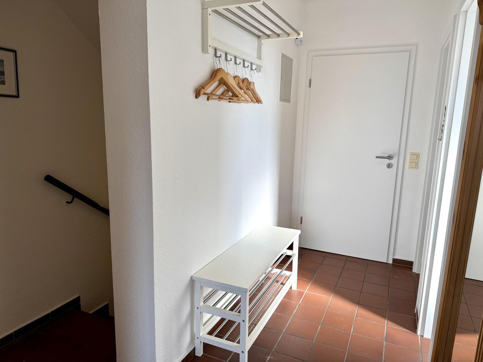 Eingangsbereich mit Hocker, Wandschrank und Holzständer.