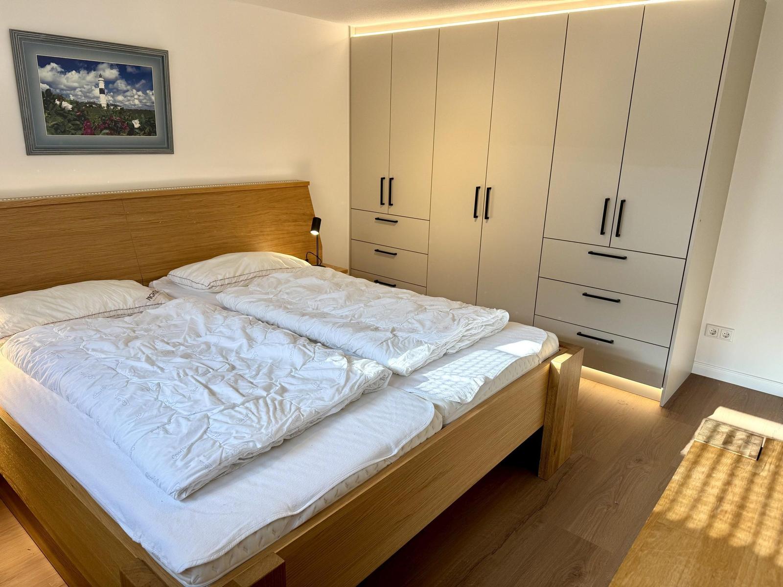 Schlafzimmer mit Doppelbett, Kleiderschrank und Wandbild.