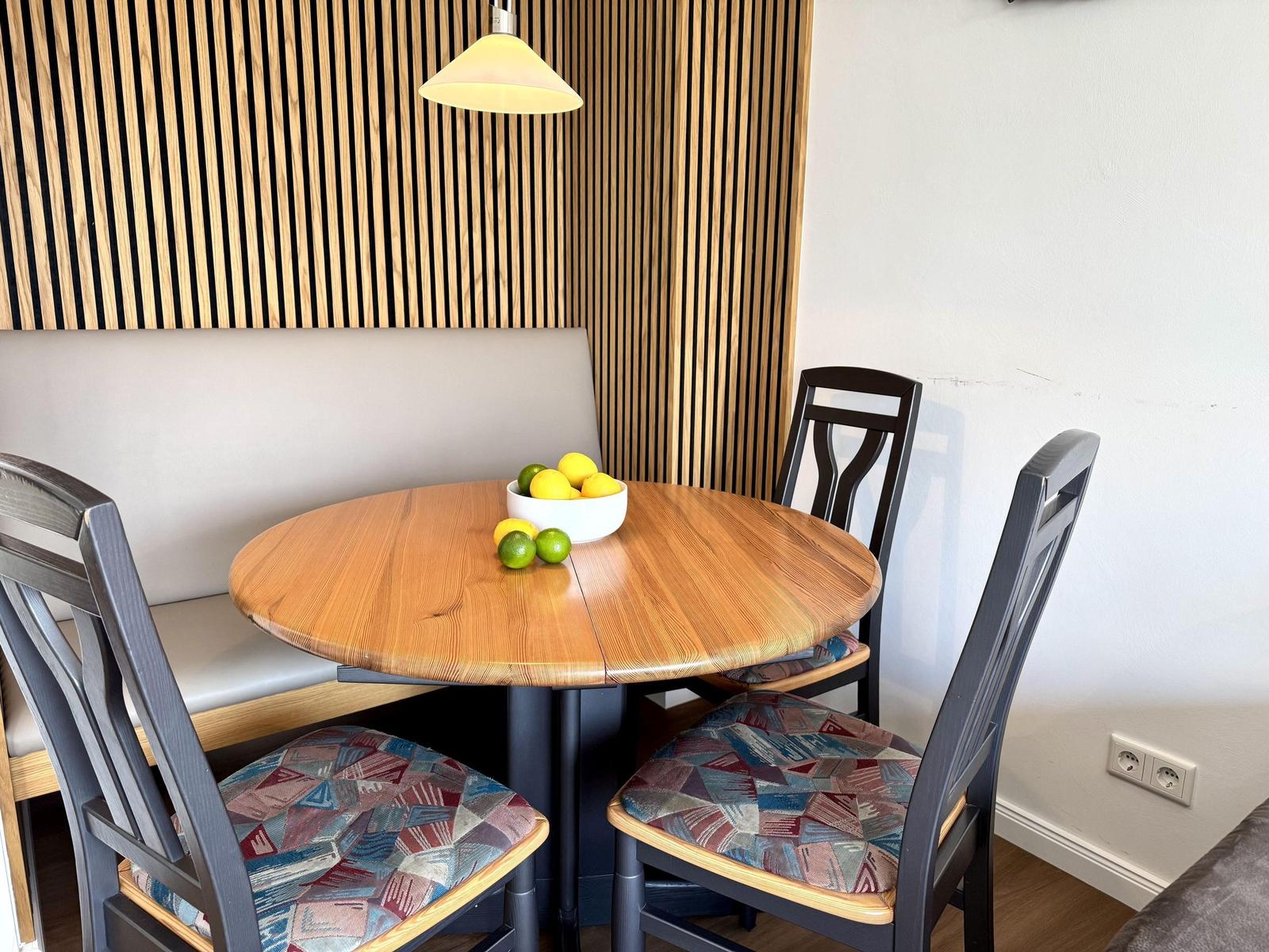 Runder Holztisch mit Stühlen und Sitzbank an Holzwand.