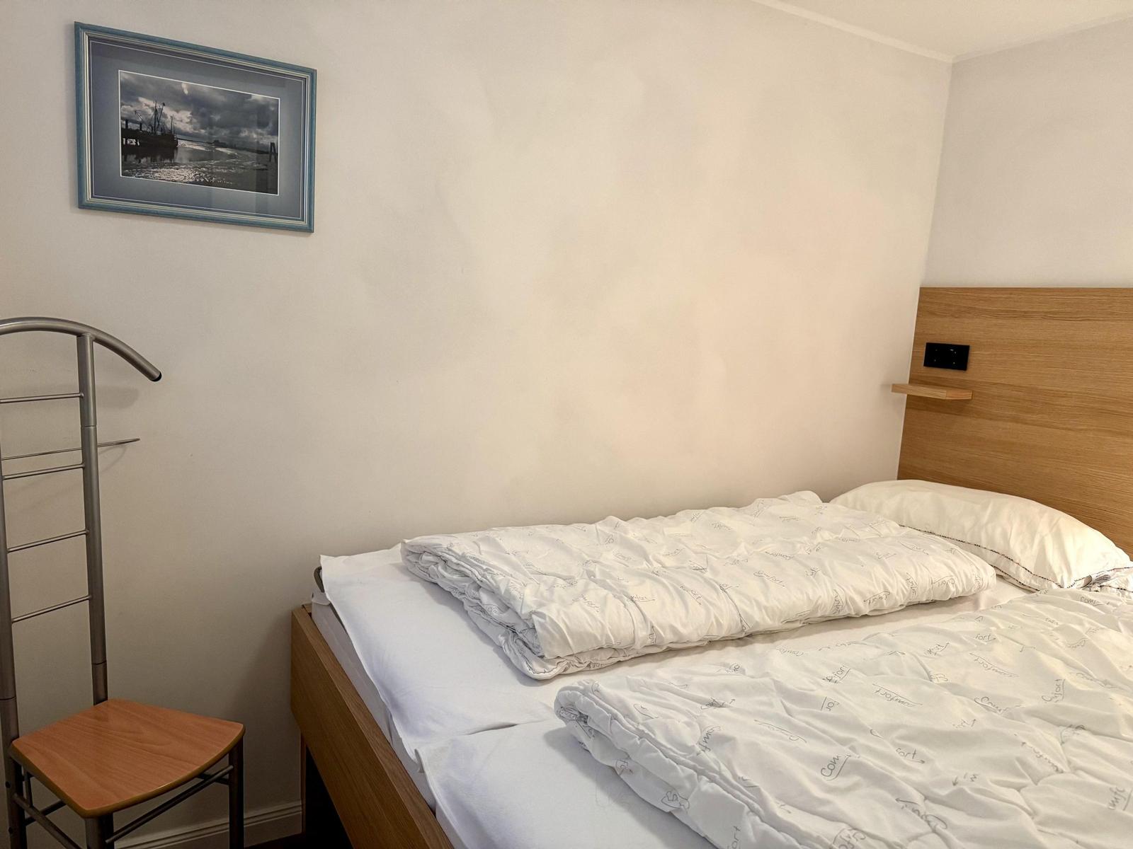 Schlafzimmer mit Bett, Wandbild und Kleiderständer.