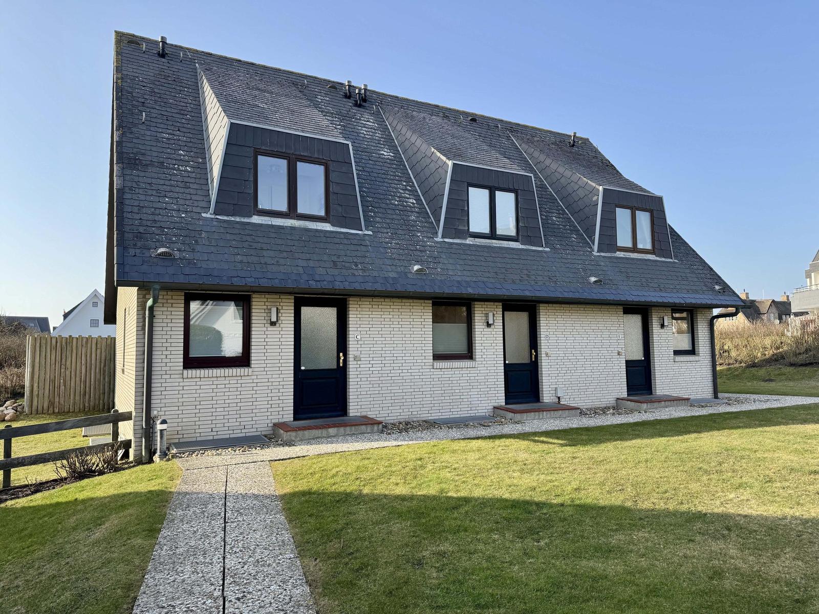 Ferienhaus mit drei Eingängen und Dachfenstern, weiß verputzt mit dunklem Dach.