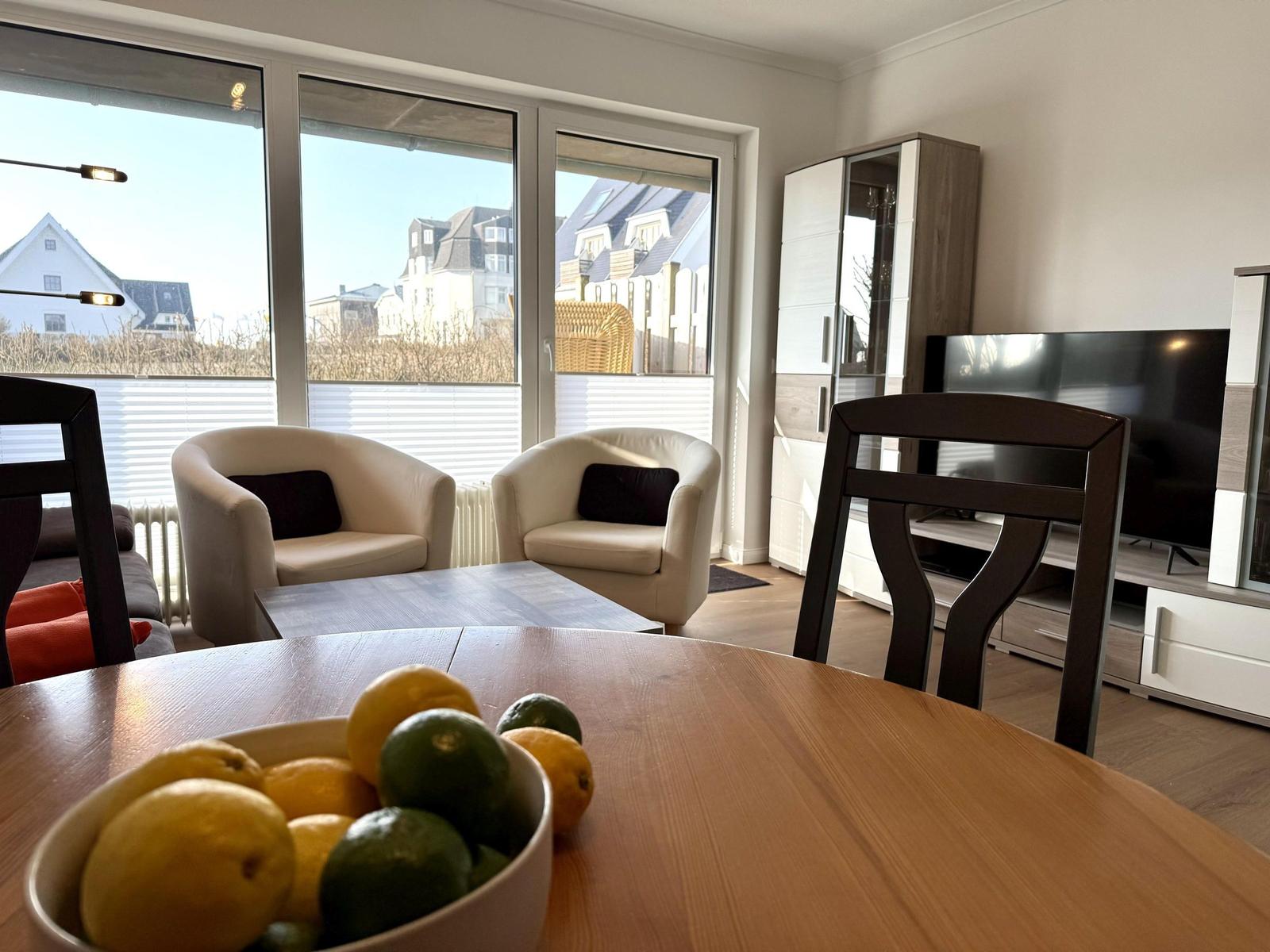 Esszimmer mit Blick auf Wohnbereich und TV. Tisch mit Obst und Sitzgelegenheiten.