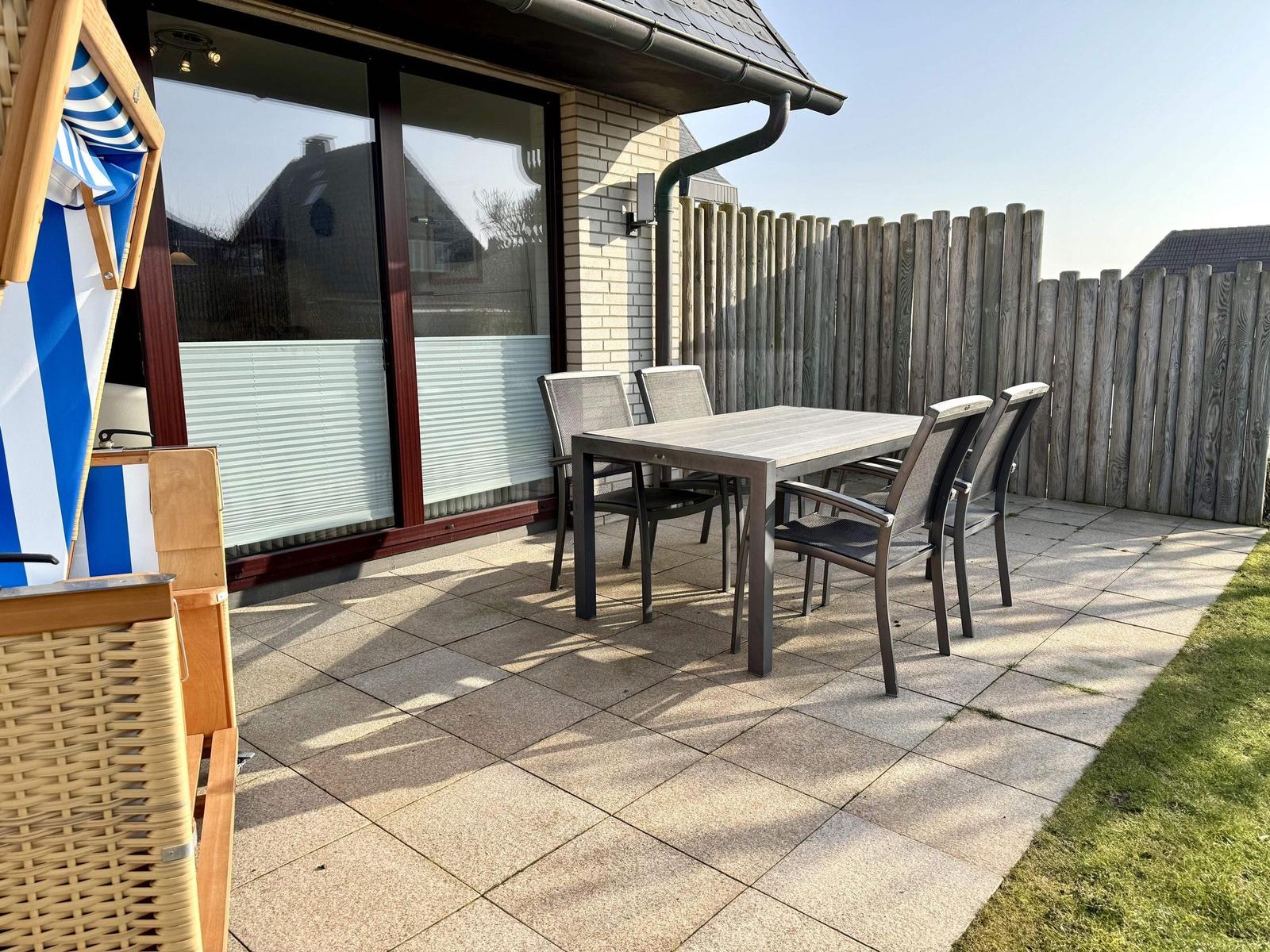Terrasse mit Tisch, Stühlen und Sonnenschirm. Hinterhof mit Holzzaun.
