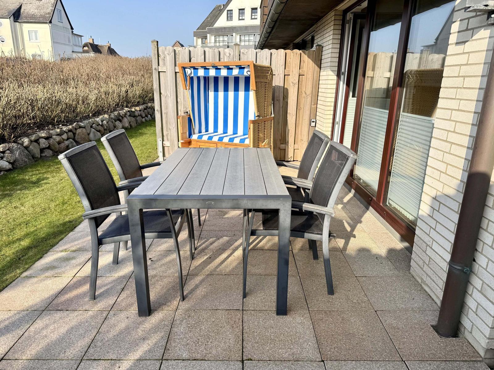 Terrasse mit Tisch, vier Stühlen und Strandkorb.