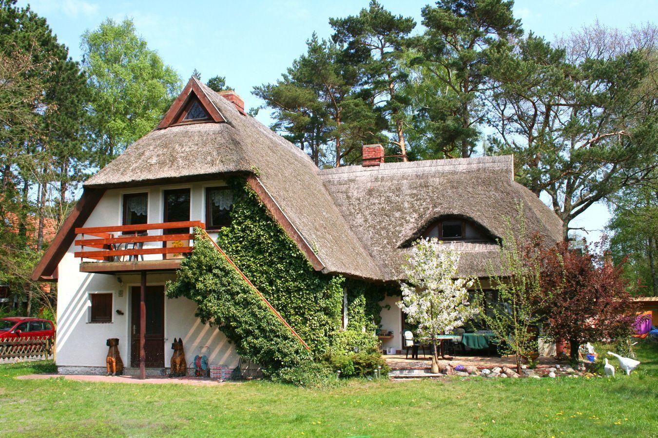 Haus mit Strohdach, Balkon und Garten. Umgeben von Bäumen und Blumen.