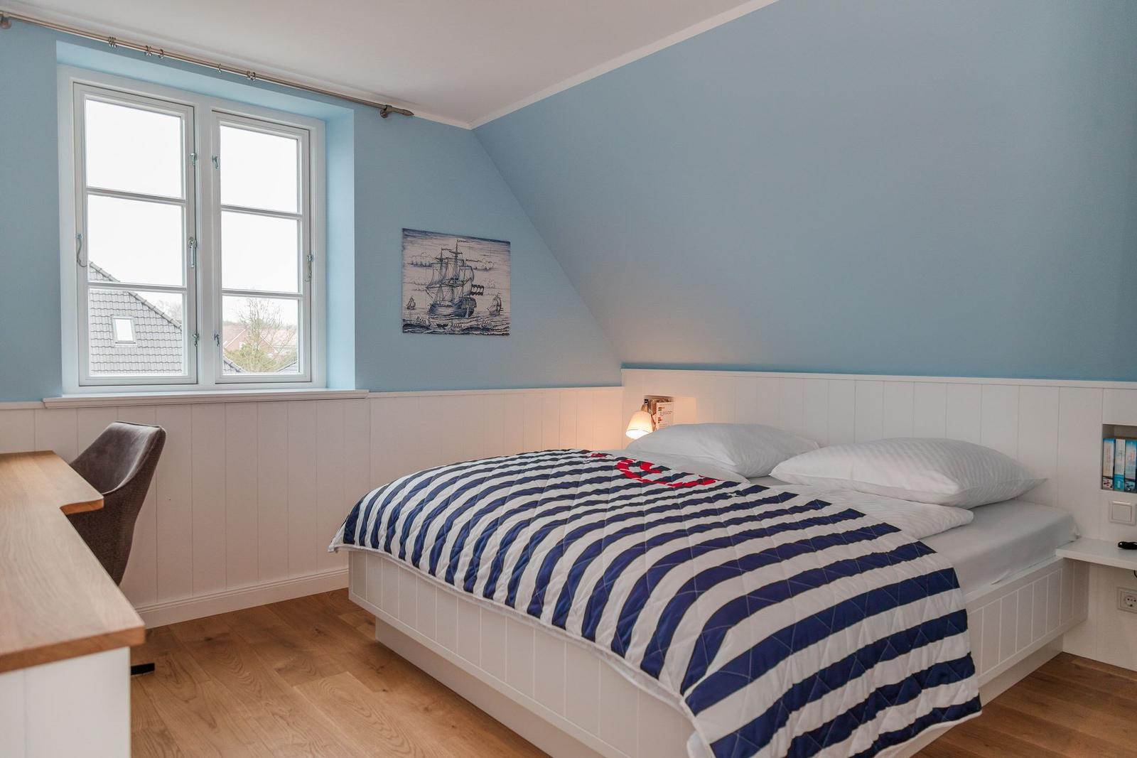 Schlafzimmer mit Bett, Fenster und Wandbild. Holzfußboden und blaue Wände.