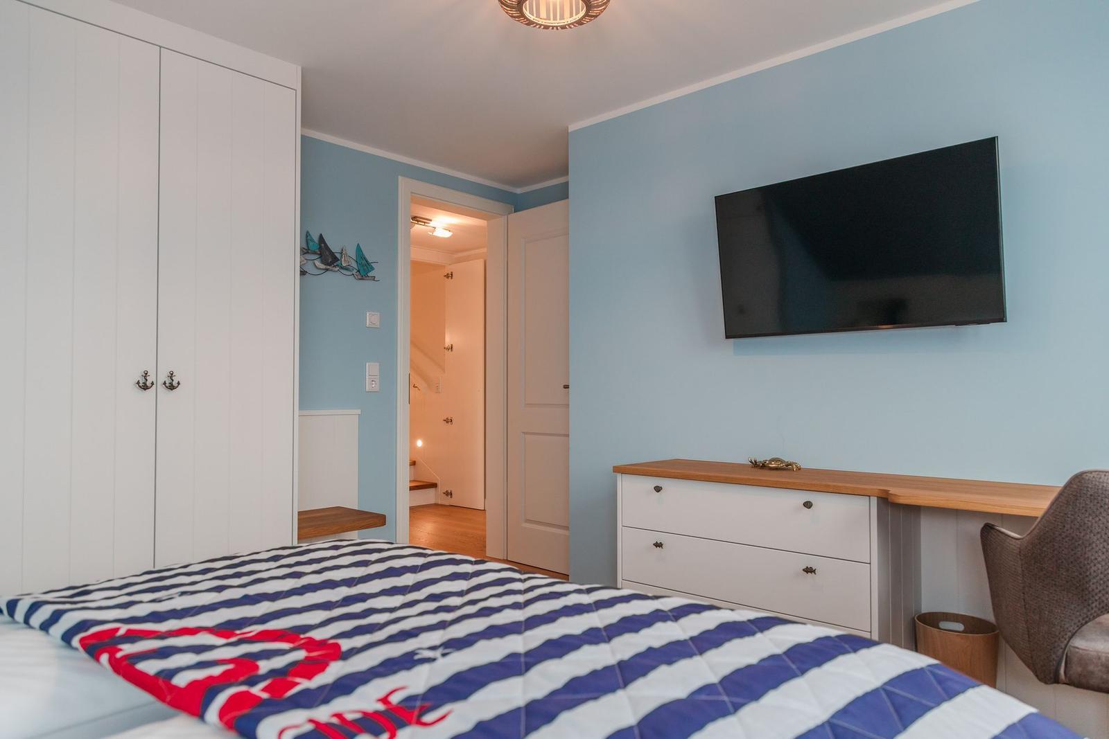 Schlafzimmer mit Bett, Kleiderschrank, TV und Schreibtisch.