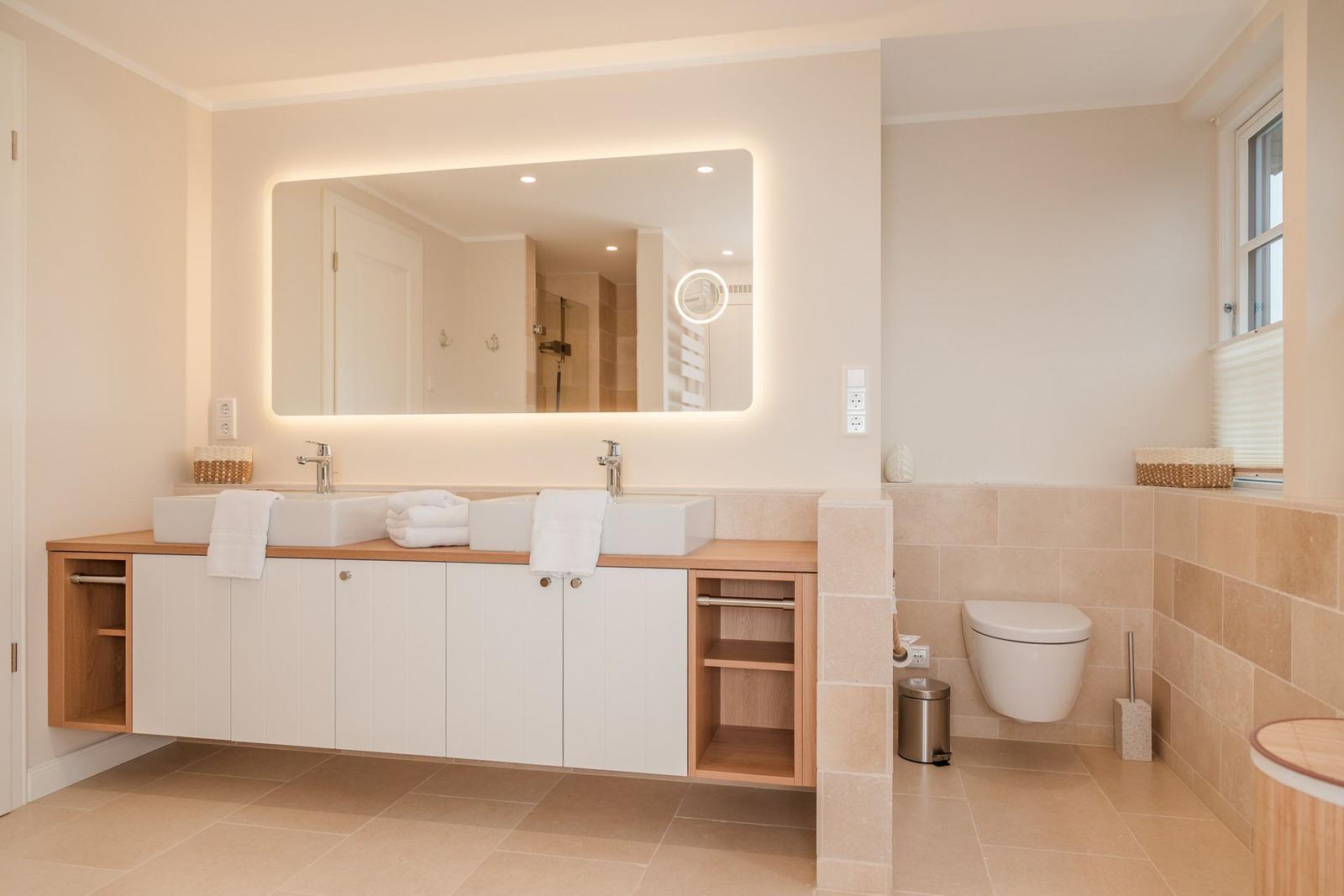 Badezimmer mit Doppelwaschbecken, beleuchtetem Spiegel und Toilette.