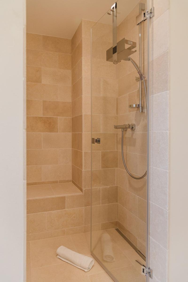 Dusche mit Glaswand, Steinfliesen und Handbrause.