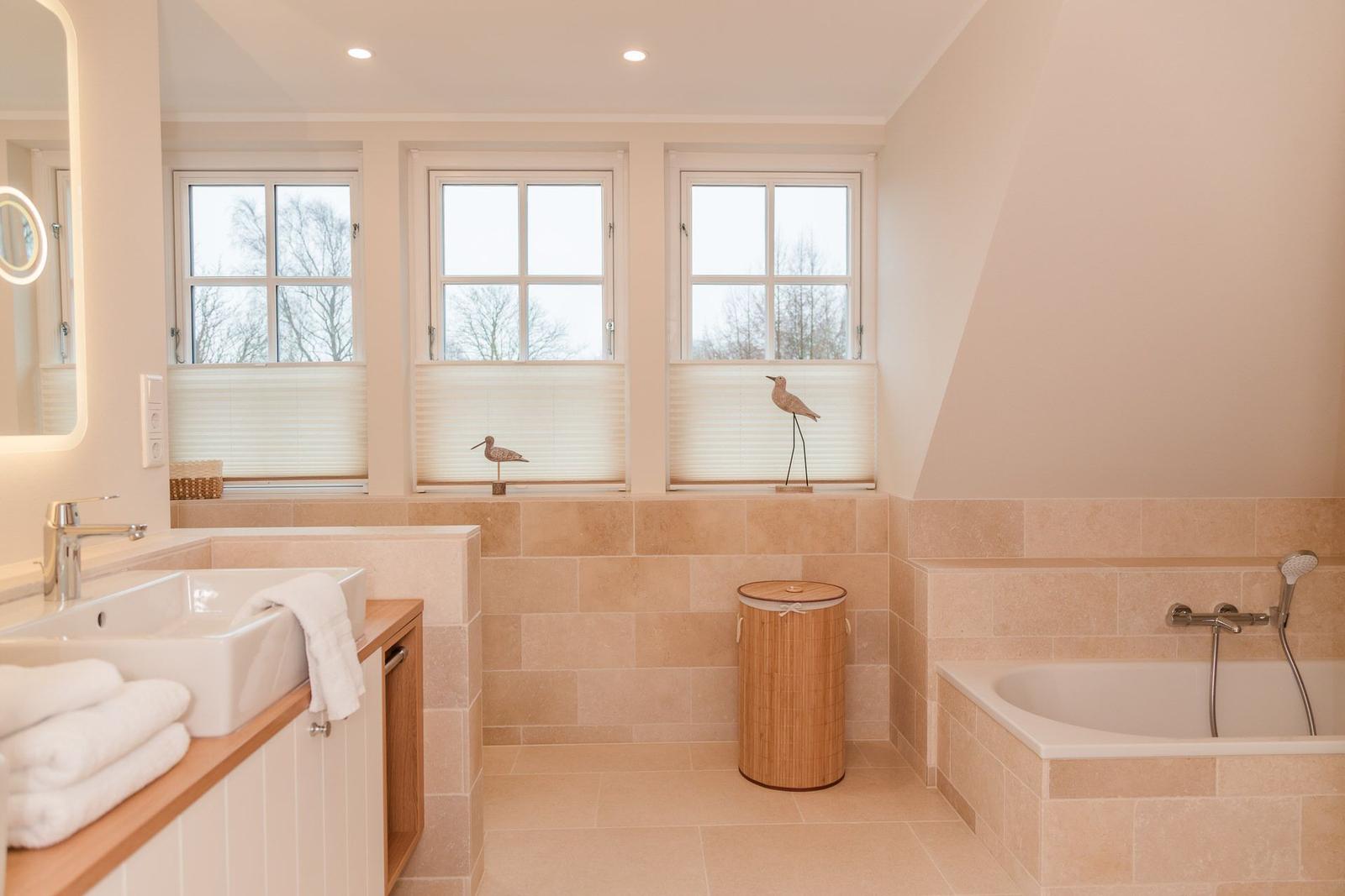 Badezimmer mit Badewanne, Waschbecken und drei Fenstern mit Jalousien.