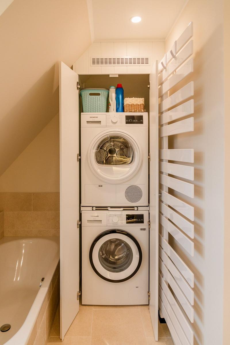 Wäschetrockner und Waschmaschine in einem Schrank neben einer Badewanne.