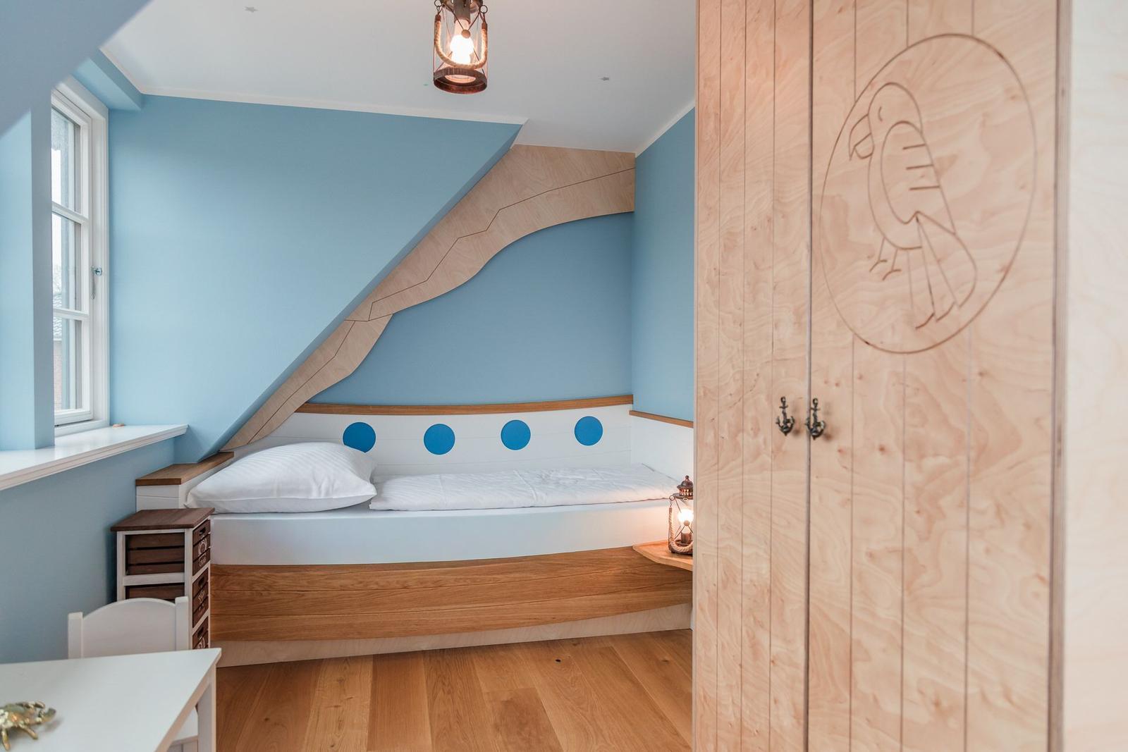 Schlafzimmer mit Bett unter Dachschräge, Holzschränkchen und Fensterbank.