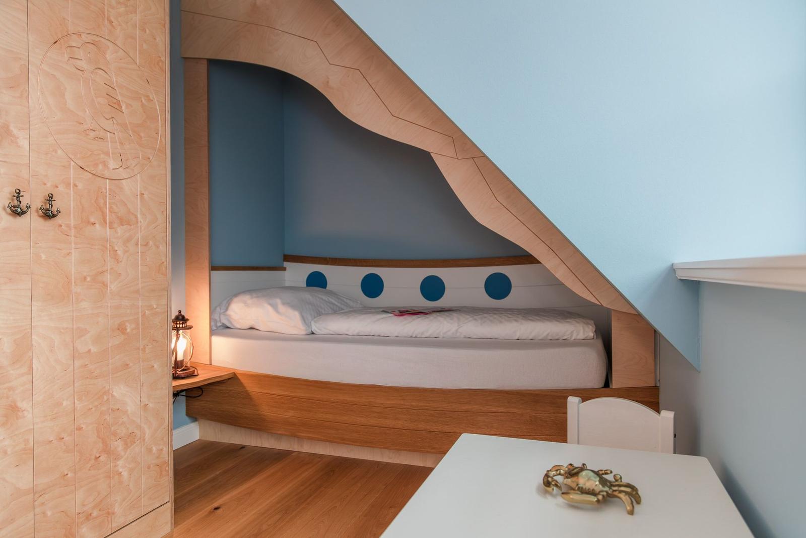 Schlafzimmer mit Bett unter Dachschräge, Holzmöbel und blauer Wand.